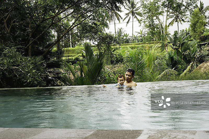 在印度尼西亚巴厘岛乌布热带森林中享受户外无边泳池的亚洲家庭图片素材