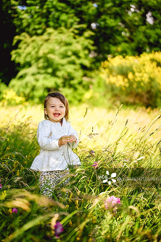 快乐的童年：小女孩在开满野花的草地上微笑图片素材