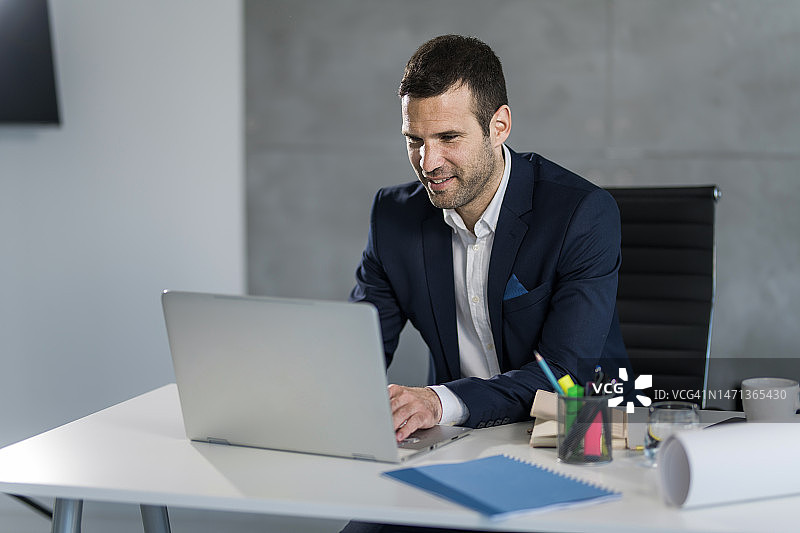 快乐的商人在办公室用笔记本电脑在线工作图片素材