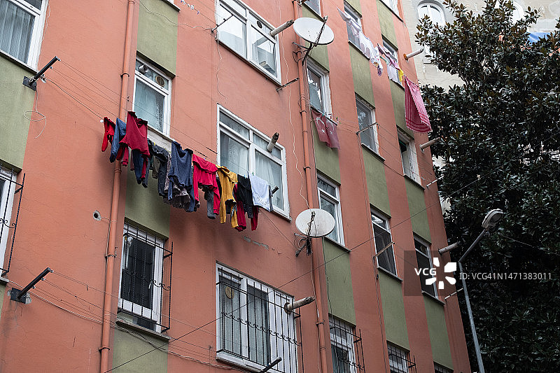 晾晒在绳子上的干净毛衣、裤子和T恤，背景是住宅楼。晾衣绳上晾晒着洗干净的男女士和儿童的衣服及床单。家务的概念。图片素材