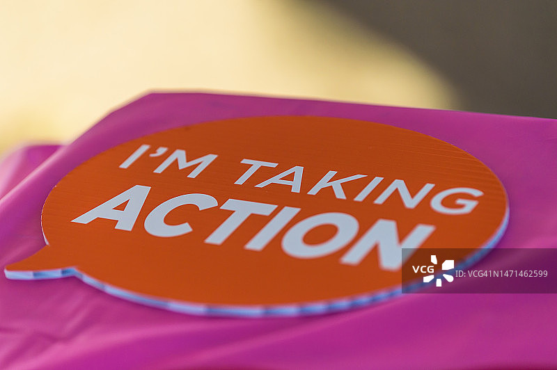 粉色桌布上的橙色纸板展示牌，写着“我正在采取行动”，在乳腺癌意识社区步行活动中图片素材