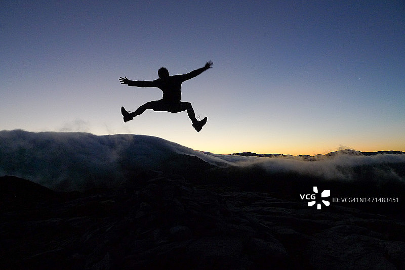 新西兰，日出时分在云层上跳跃的人物剪影图片素材