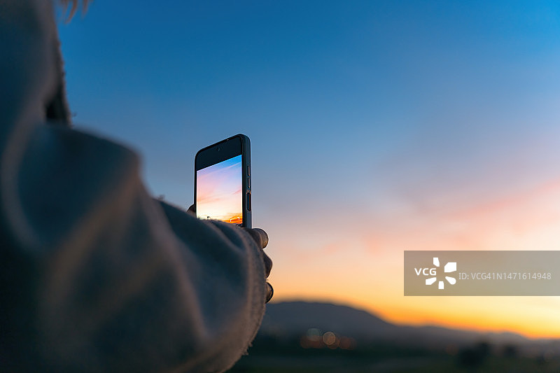 年轻女子用手机拍摄日落美景图片素材