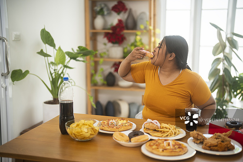 我看到一个亚洲胖女孩在桌子旁狼吞虎咽地吃垃圾食品图片素材