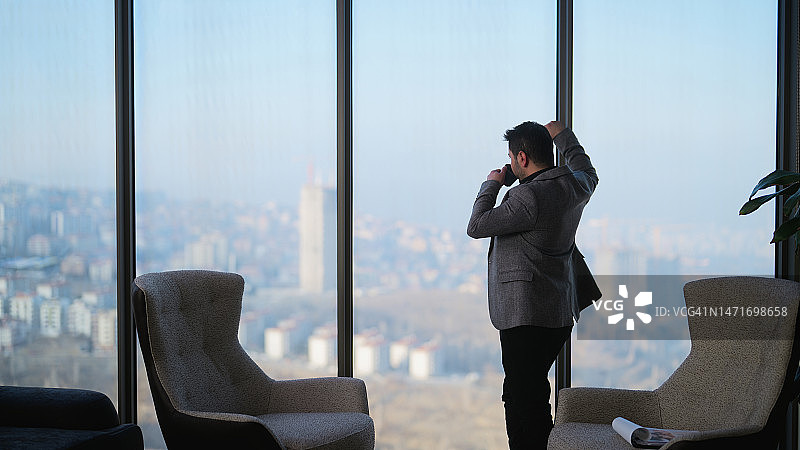 在现代办公室里休息、喝热饮并眺望窗外的年轻商人图片素材