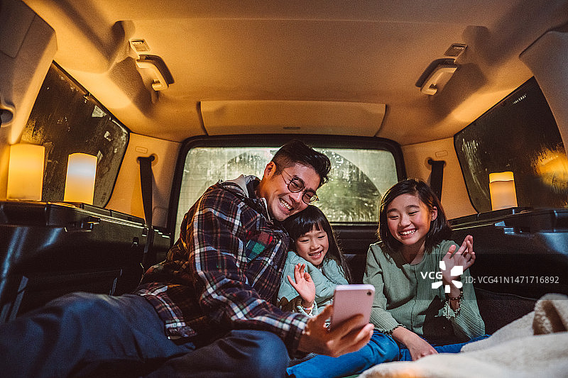 父亲和女儿在汽车后备箱露营时用智能手机愉快地进行视频通话图片素材