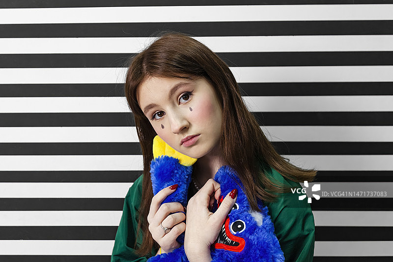 可爱的女孩在黑白条纹房间里哭泣，手里拿着一个毛绒玩具图片素材