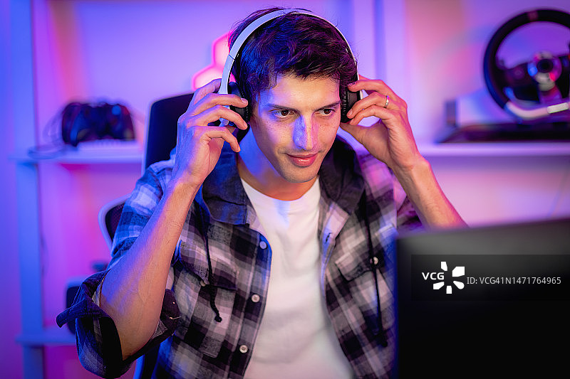 在激动人心的霓虹灯气氛中流媒体播放前戴着耳机的男性网红游戏玩家，科技概念，娱乐图片素材