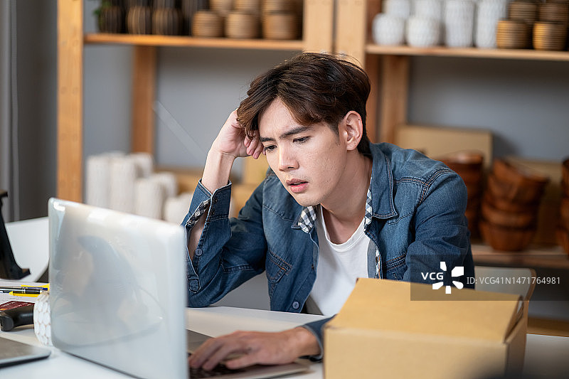 年轻的亚洲男人在网上销售花瓶，因在线销售额下降而在笔记本电脑前感到压力图片素材