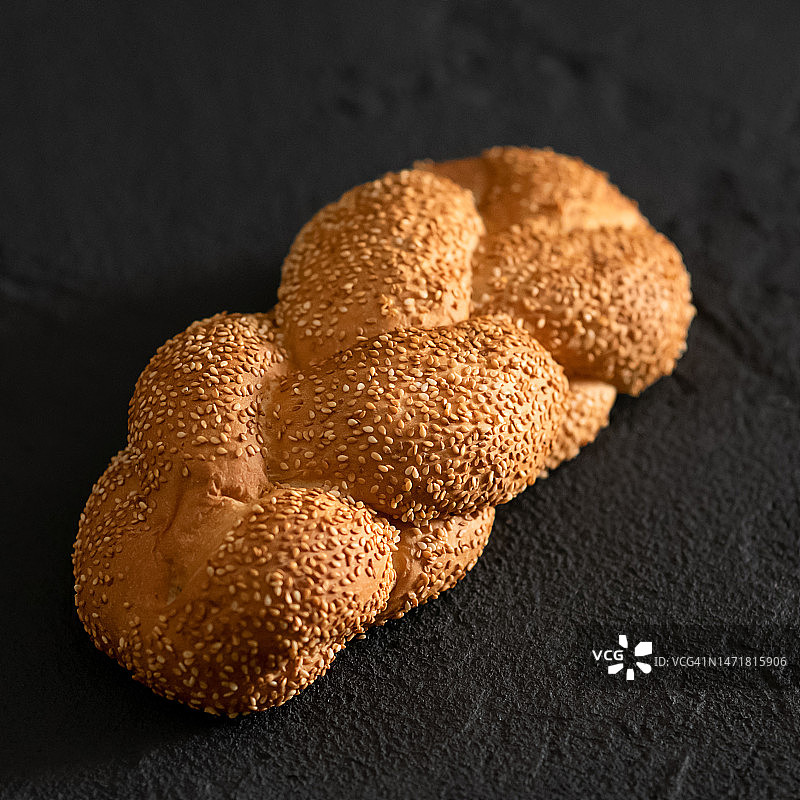 撒有芝麻的辫状小麦粉面包，深灰色背景上的整条白面包，顶部视角，柔焦图片素材