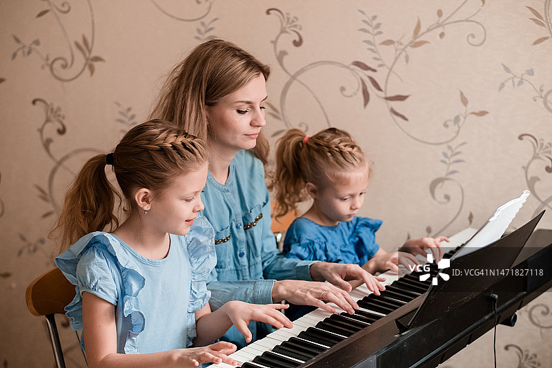 母亲和两个金发女儿在家看乐谱弹钢琴图片素材