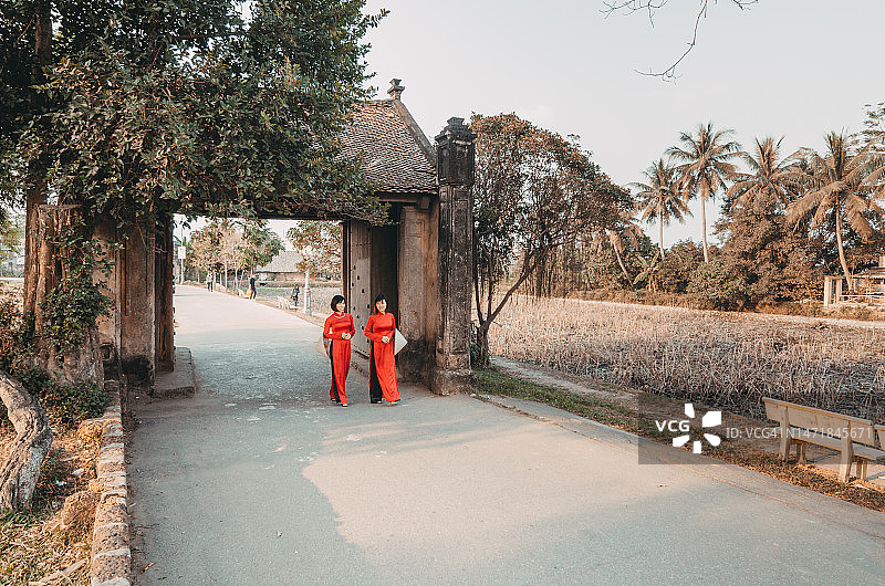 两位年轻女士身穿越南红色奥黛，走过古老的Duong Lam大门图片素材