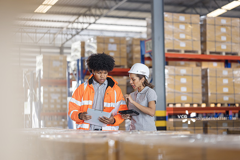 专用信息共享易于跟踪仓库运营中的库存位置和水平。男女仓库员工在物流仓库中讨论平板电脑，以跟踪库存平衡图片素材