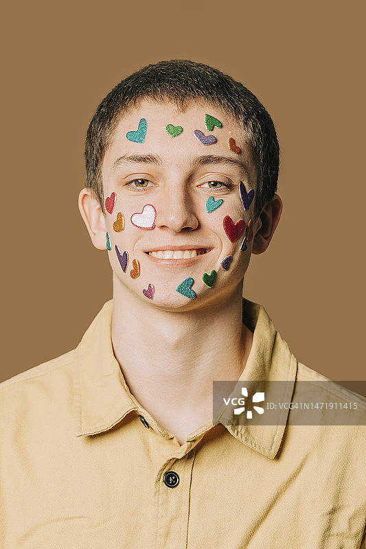 快乐的青少年男孩在棕色墙前脸上贴着心形贴纸图片素材