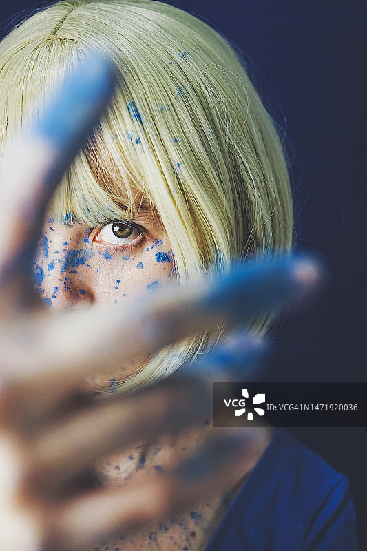 透过蓝色油漆手指看东西的金发女人图片素材
