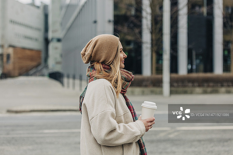 微笑的女人穿着暖和的衣服拿着一次性杯子图片素材