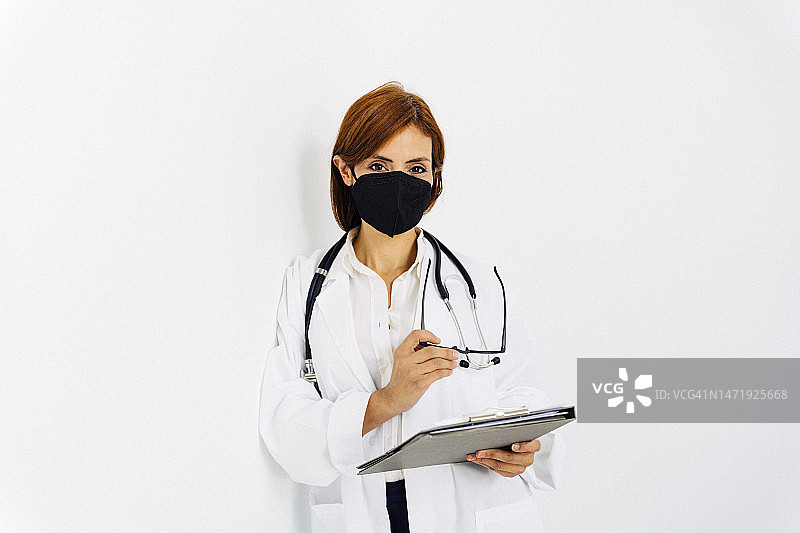 戴眼镜和拿着剪贴板的女医生靠在墙上图片素材