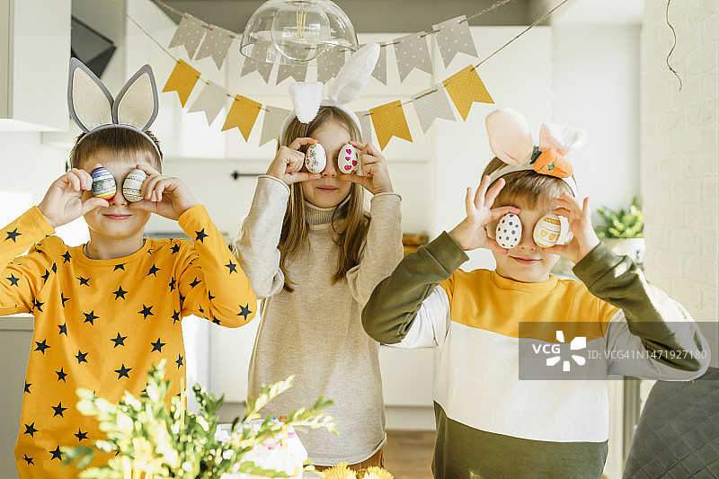 孩子们在家手拿复活节彩蛋遮眼微笑图片素材