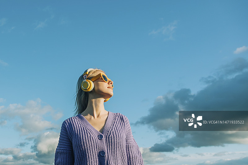 在蓝天下戴无线耳机听音乐的女人图片素材