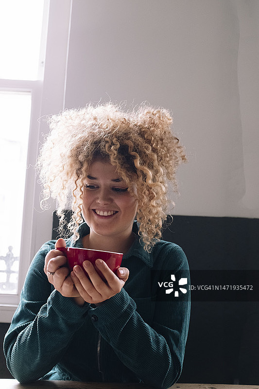 快乐的女商人拿着咖啡杯坐在办公室里图片素材