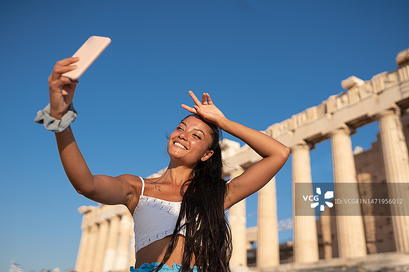 微笑的亚洲女旅行者在希腊雅典卫城前用手机自拍图片素材