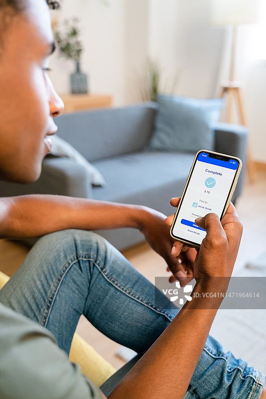 匿名男子坐在沙发上用智能手机汇款的侧视图图片素材