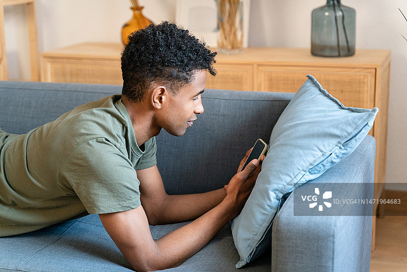 非裔美国男子躺在沙发上看手机视频图片素材
