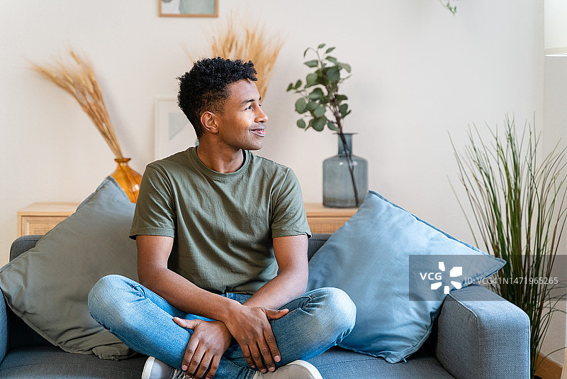 穿着休闲装坐在沙发上，在舒适的客厅里休息并看向镜头的年轻男人图片素材