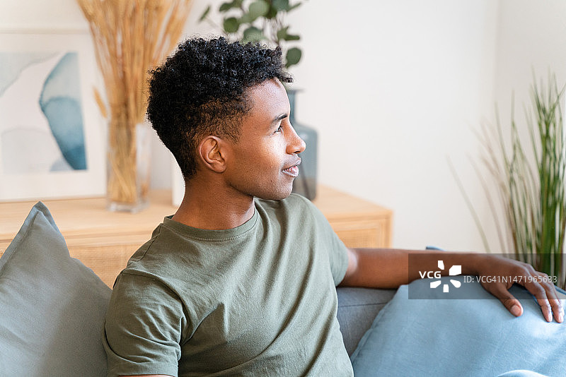 穿着休闲装坐在沙发上，在舒适的客厅里休息并看向镜头的年轻男人图片素材