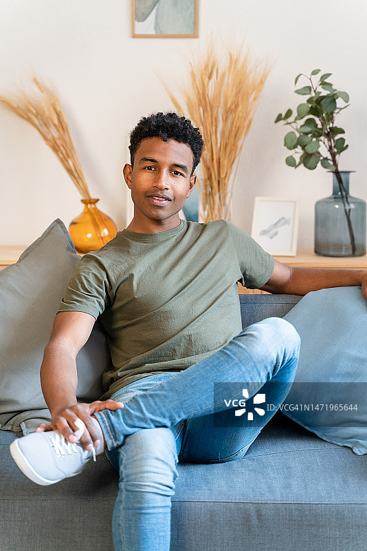 穿着休闲装坐在沙发上，在舒适的客厅里休息并看向镜头的年轻男人图片素材
