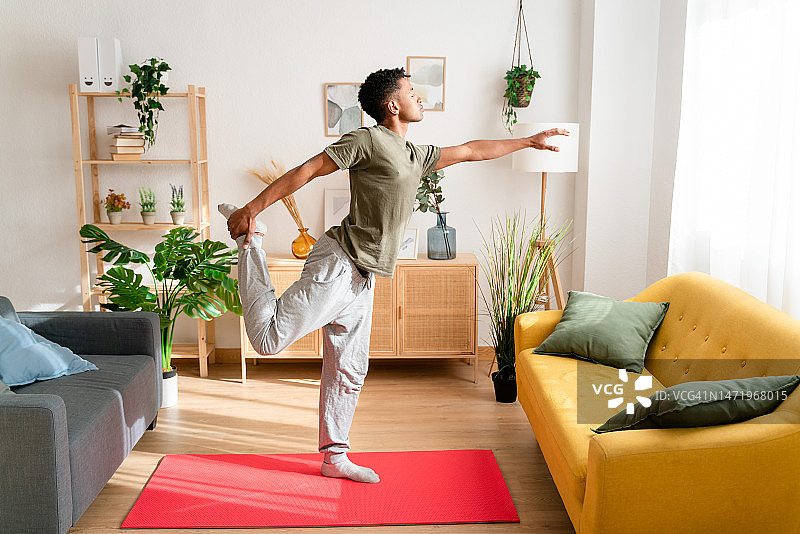 快乐的男人在现代舒适的客厅里享受周末早晨，赤脚在沙发床上伸展身体，充满活力地进行健身活动图片素材