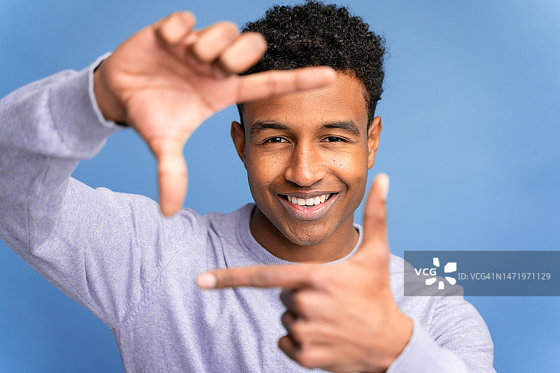 穿白衬衫的非裔美国男人面带微笑，站在蓝色演播室背景前看着镜头图片素材