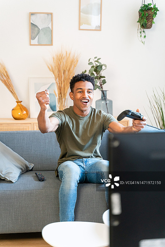 非裔美国男人坐在沙发上玩电子游戏图片素材