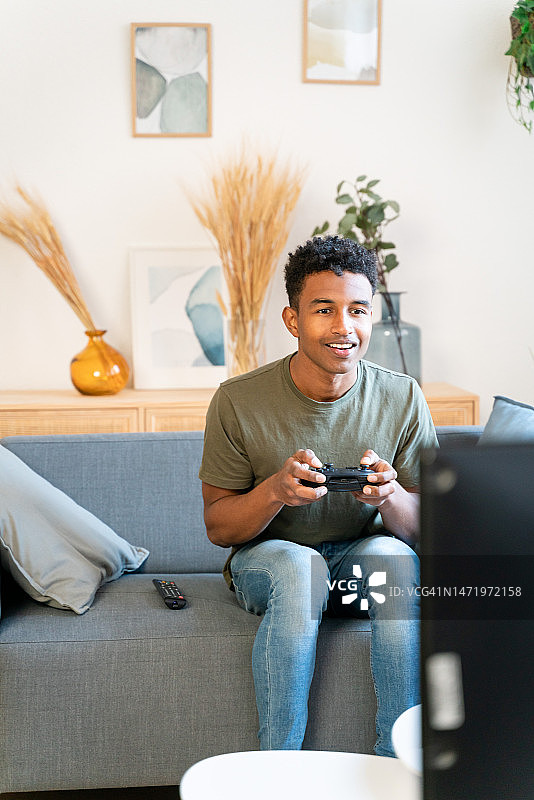 平静的非裔美国男子坐在沙发上，在家中舒适的客厅里玩电子游戏图片素材