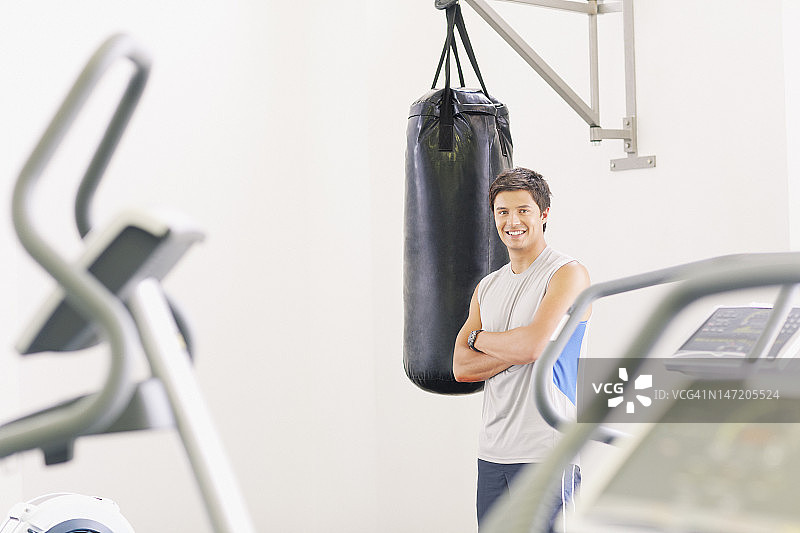 在健身房站在拳击沙袋旁的微笑男人肖像图片素材