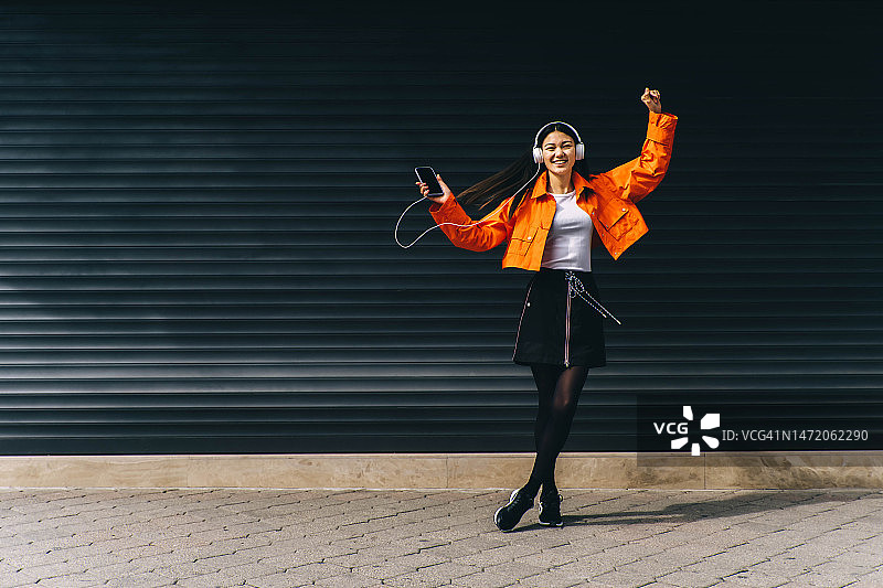 黑色背景下，穿着橙色夹克、戴着白色耳机的亚洲舞蹈美女肖像图片素材