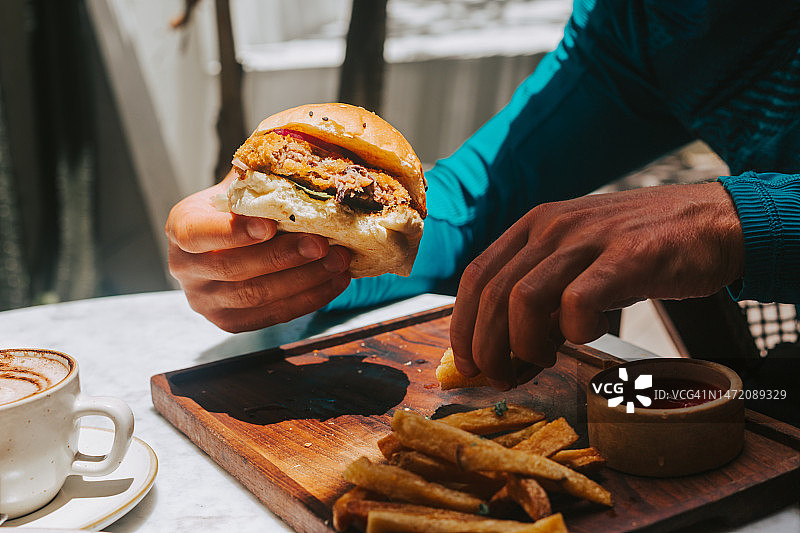 手持纯素汉堡，将炸薯条蘸入酱汁图片素材