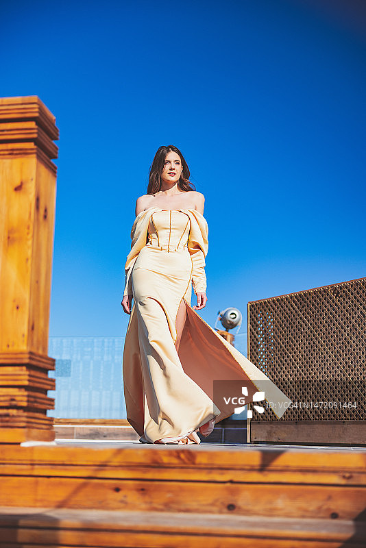 穿着米色露肩连衣裙的年轻女子站在夏日木制楼梯上图片素材
