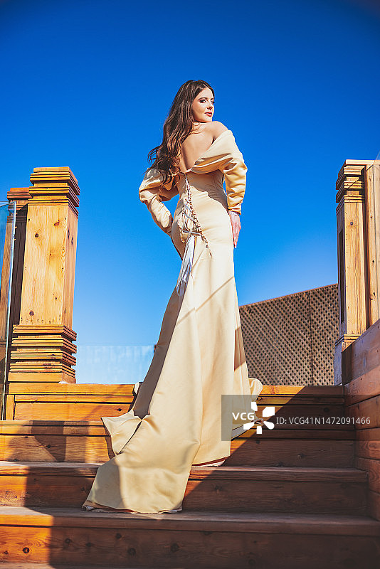 站在木质楼梯顶端的露背米色连衣裙年轻女子图片素材