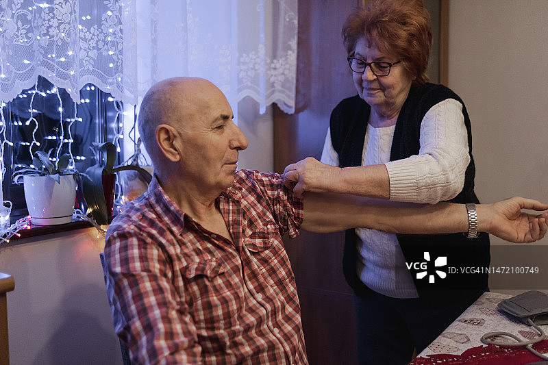 正在调整丈夫手臂上充气袖带的年长女性图片素材