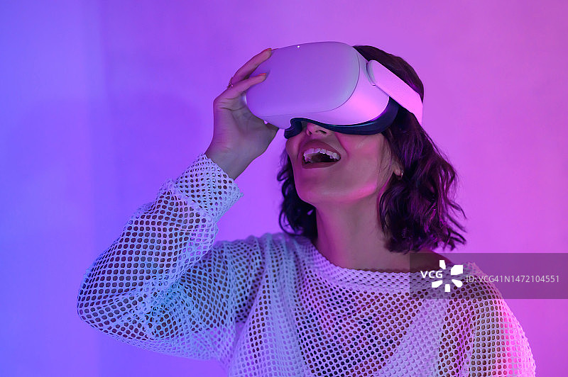 在紫色和粉色空间中戴VR头显的快乐女性特写图片素材