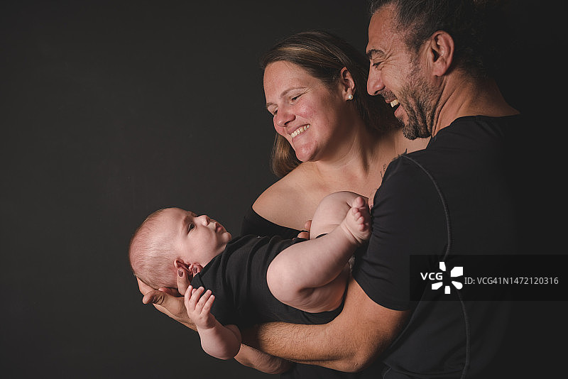 父母在黑色背景上拥抱小男婴的影棚照片图片素材