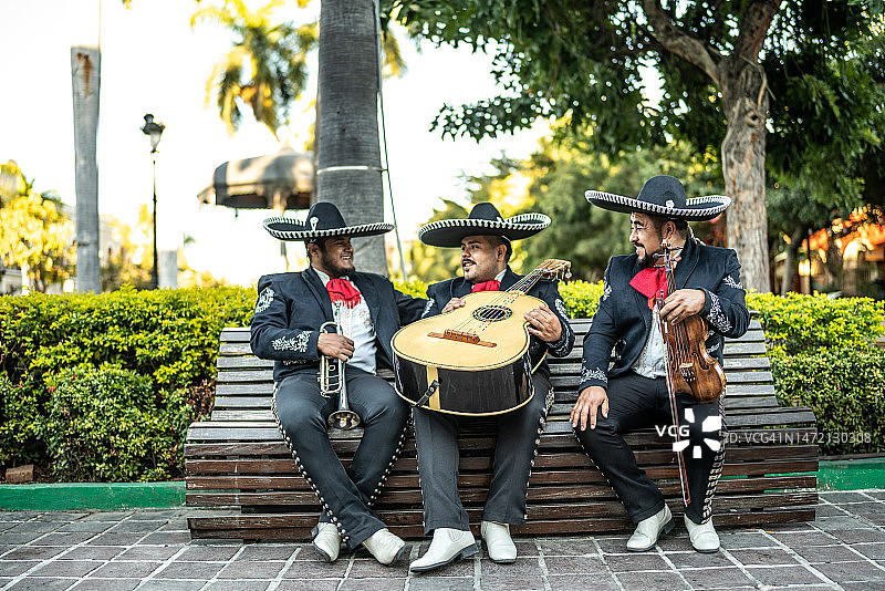 坐在户外长凳上的三位传统墨西哥流浪乐队乐手图片素材
