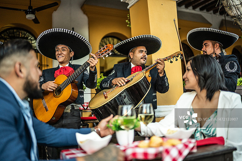已婚夫妇在户外餐厅享用晚餐，欣赏墨西哥流浪乐队的音乐图片素材