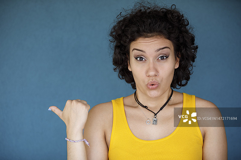 兴奋的年轻女人用手指指着蓝色背景图片素材