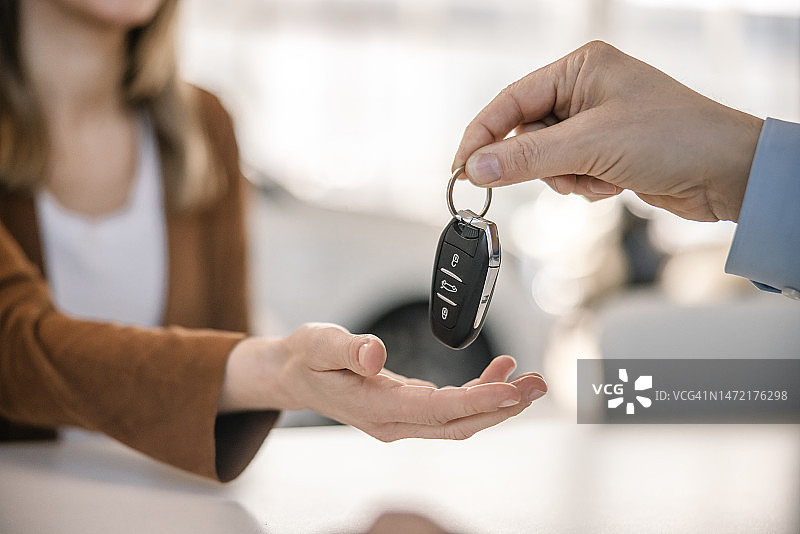汽车销售员在汽车经销商办公室里将新车钥匙交给女顾客的特写图片素材