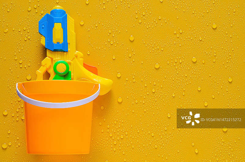 湿黄色背景上水桶里的水枪图片素材