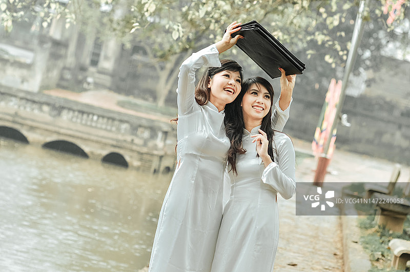 两位身穿传统奥黛、手持盛开百合的美丽温柔女学生图片素材