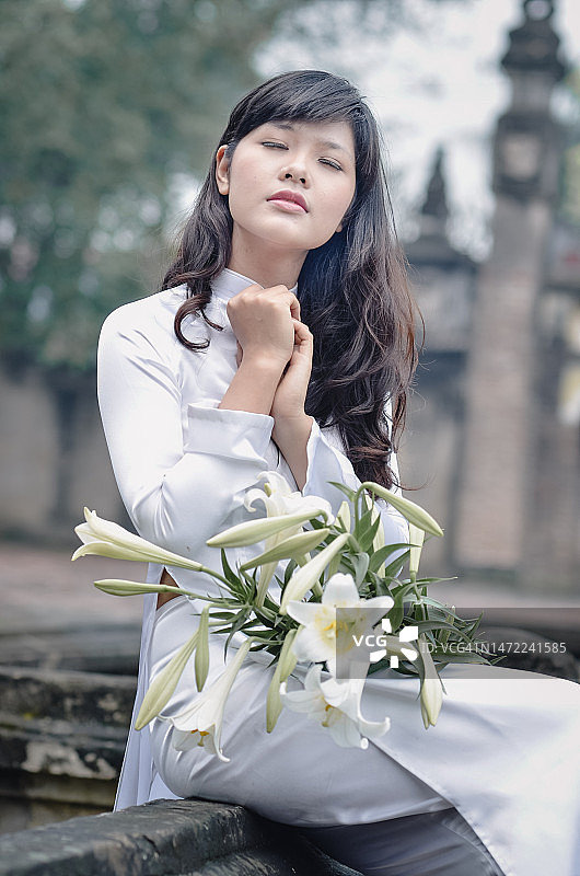 迷人的年轻越南女孩身穿传统奥黛，手持百合花图片素材