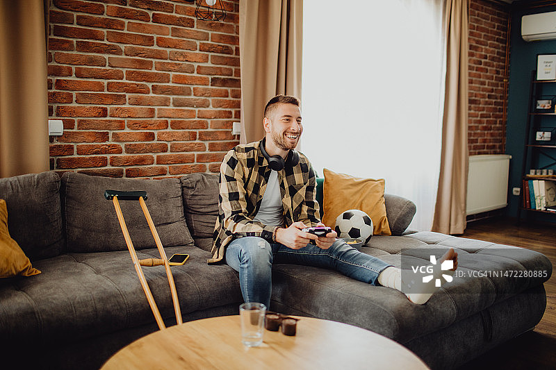 腿部受伤在家玩游戏的快乐年轻人图片素材